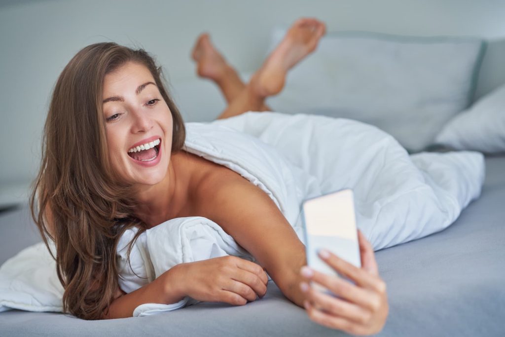 Brunette sexy girl on bed with phone smiling.